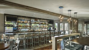 A bar area with multiple seating options, a variety of bottles and glasses on shelves, and a modern chandelier. - The Inn at Chesapeake Bay Beach Club (Stevensville)