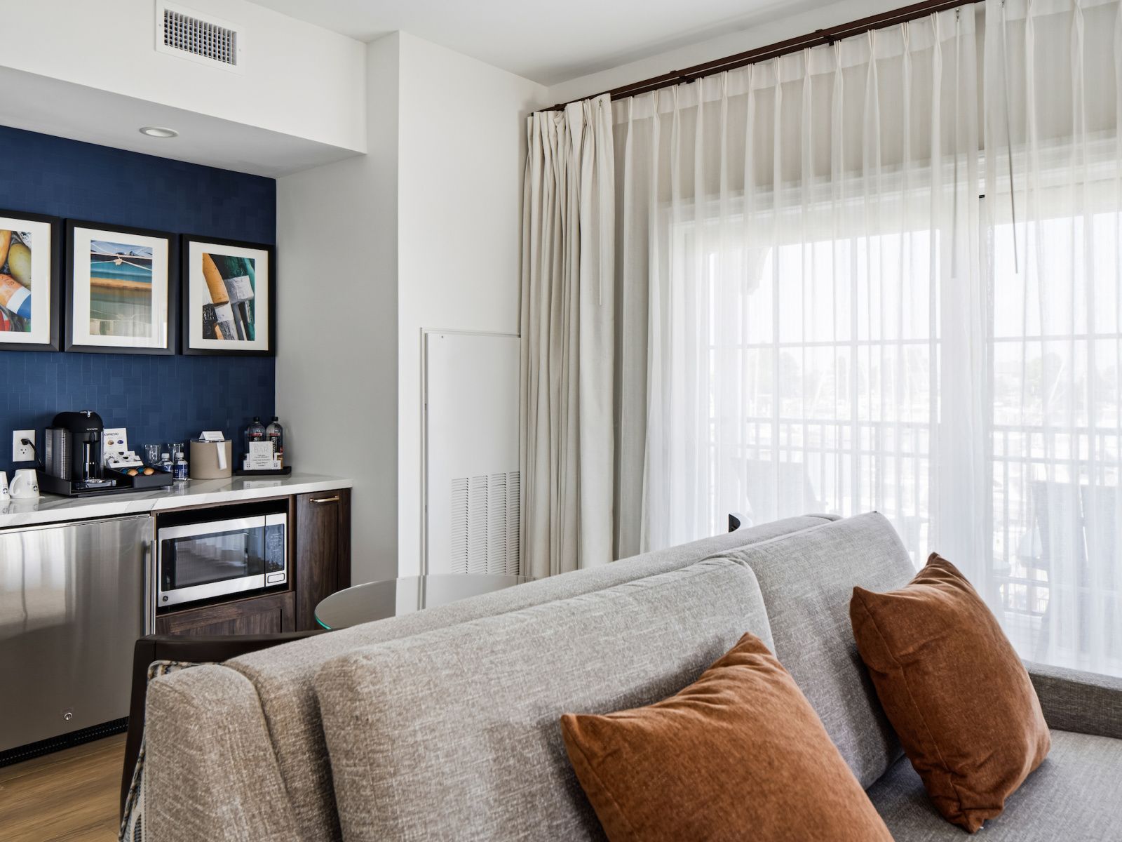 A modern hotel room with a grey sofa, a coffee station, and artwork on the wall.