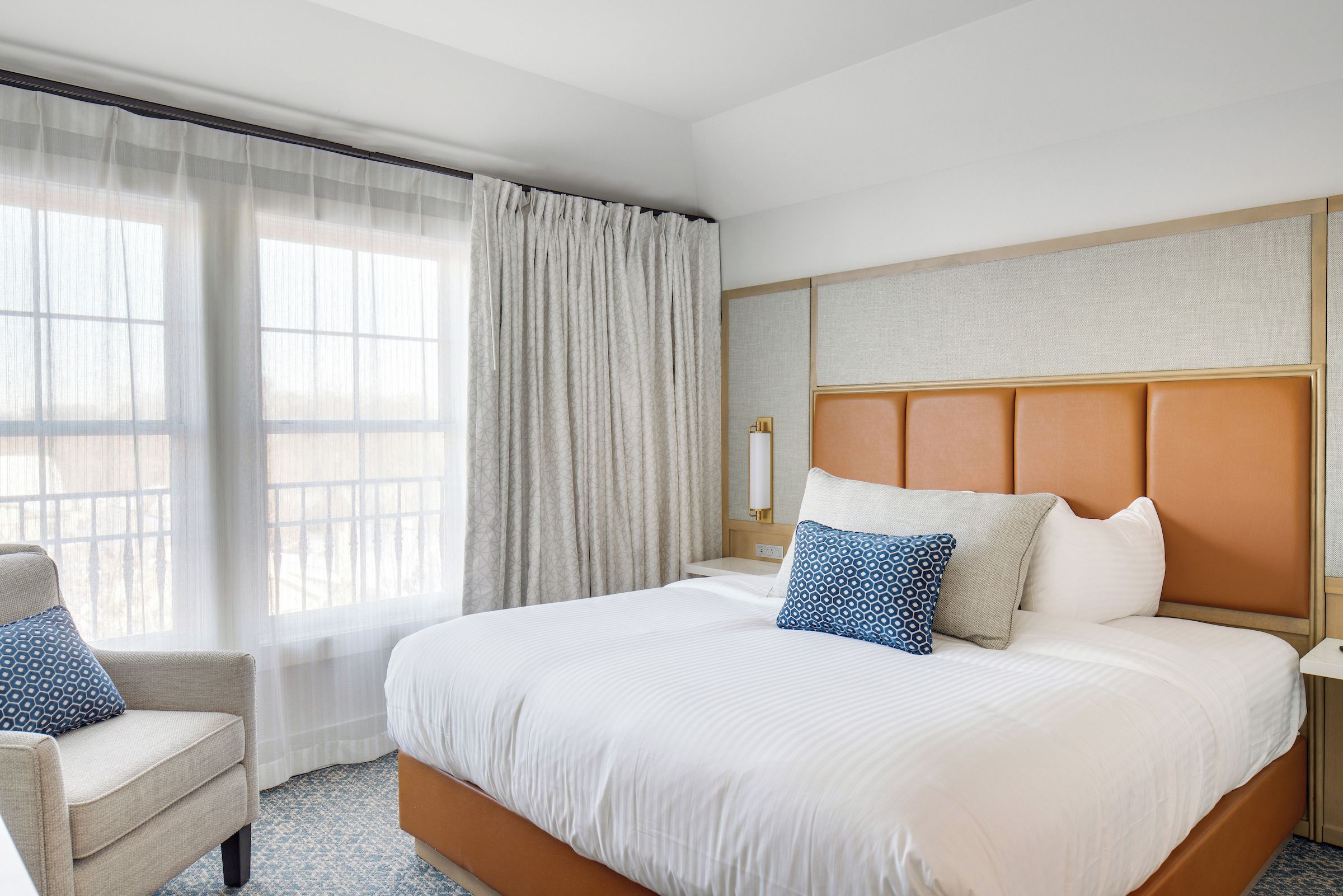 Une chambre d’hôtel avec un grand lit, une chaise, une table de chevet et une fenêtre avec des rideaux.