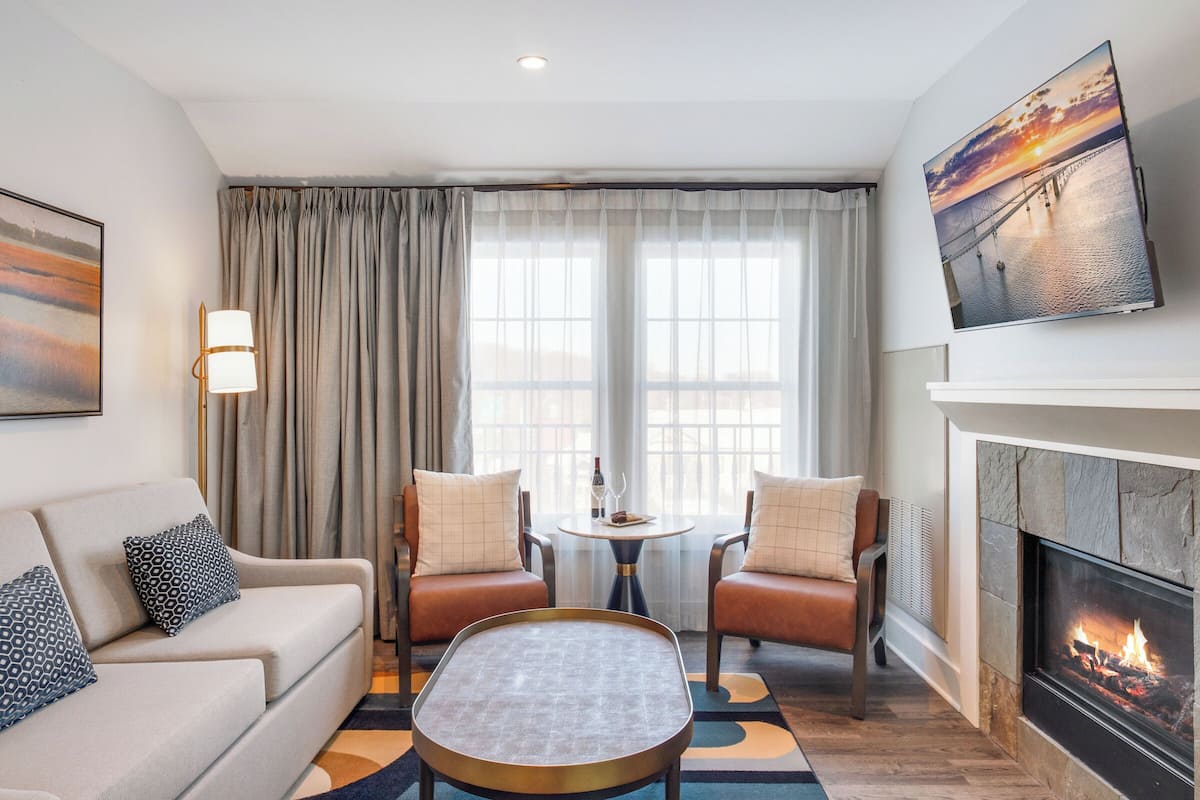 A modern living room with a sofa, two armchairs, a coffee table, a fireplace, and a large window with curtains.