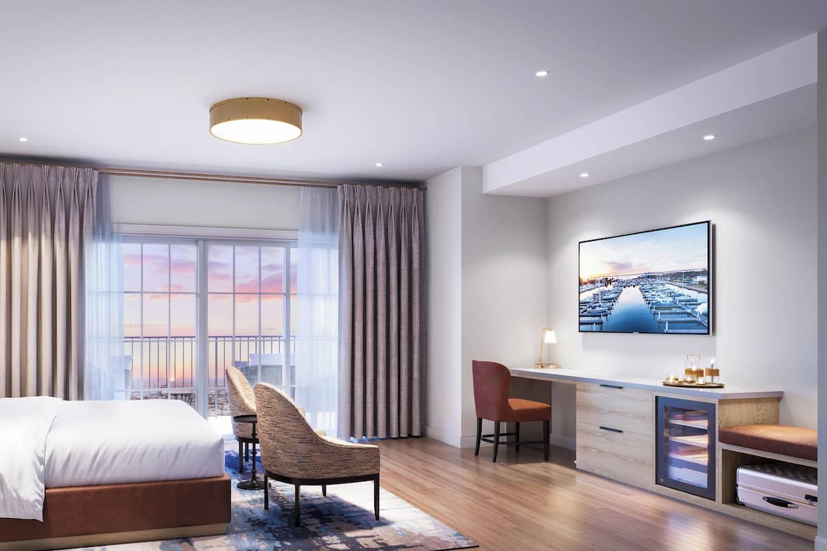 A modern hotel room with a bed, desk, chair, and large windows with curtains.