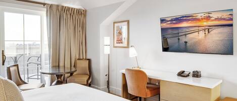 Una habitación de hotel con cama, escritorio, silla, mesa y vista a un puente al atardecer.