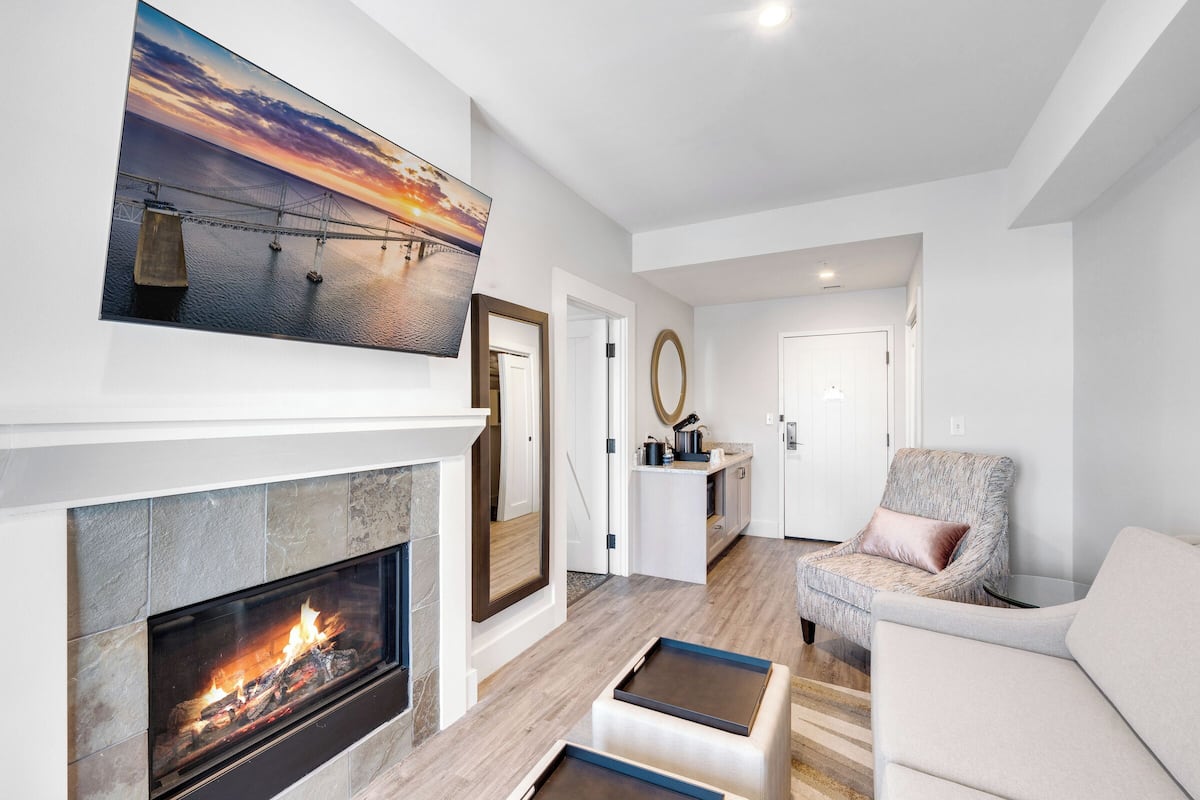A modern living room with a fireplace, a large painting of a sunset over a bridge, and a cozy seating area.