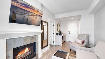 A modern living room with a fireplace, a large painting of a sunset over a bridge, and a cozy seating area.