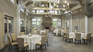 A spacious dining area with round tables, high ceilings with ductwork, and a stone fireplace. - The Inn at Chesapeake Bay Beach Club (Stevensville)