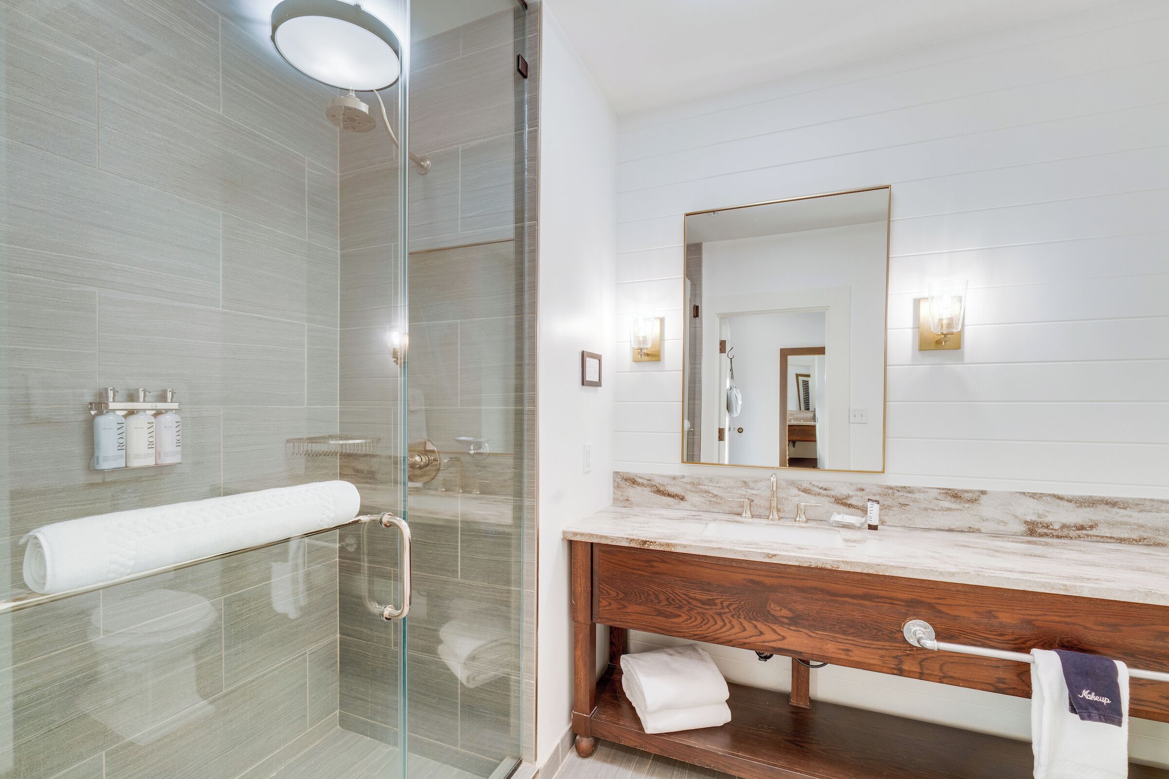 A modern bathroom with a glass-enclosed shower, a marble vanity, and a large mirror.