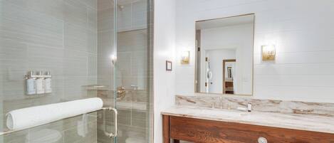 A modern bathroom with a glass-enclosed shower, a marble vanity, and a large mirror.