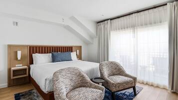 A hotel room with a bed, two armchairs, a small table, and a large window with curtains.