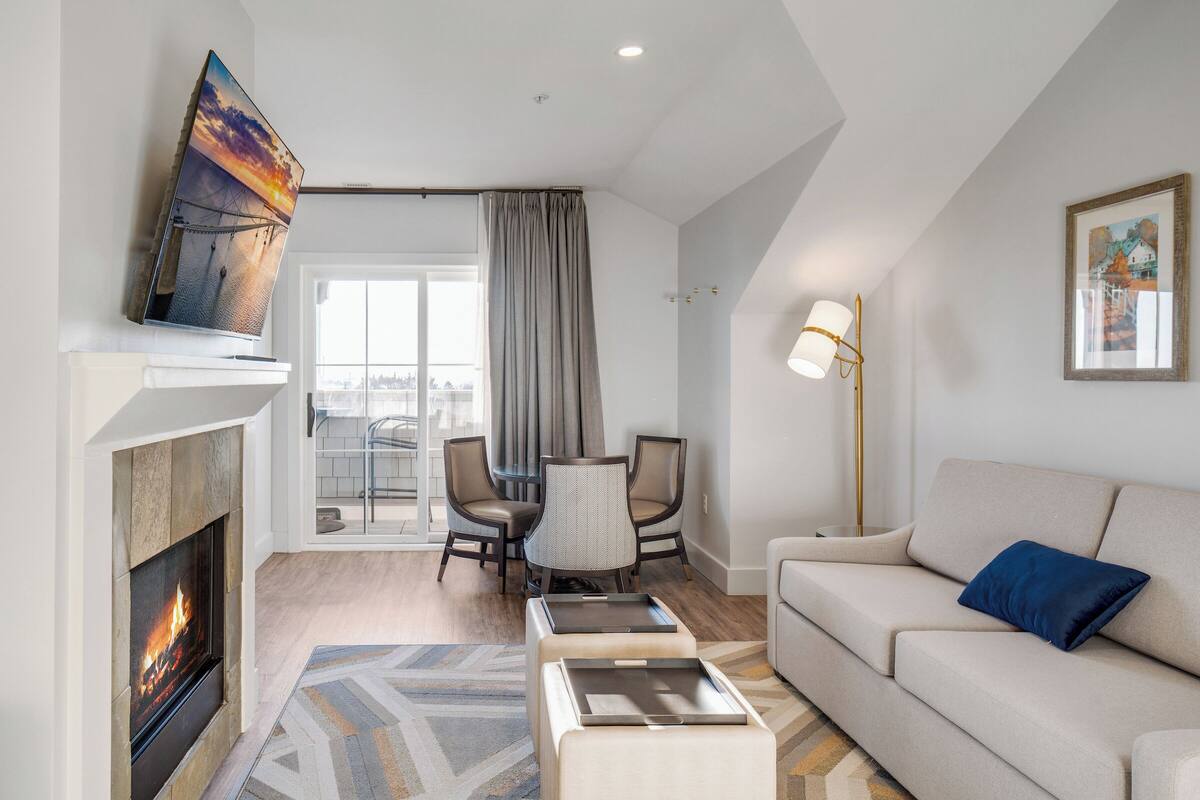 A modern living room with a fireplace, a sofa, a coffee table, and a dining area with chairs.