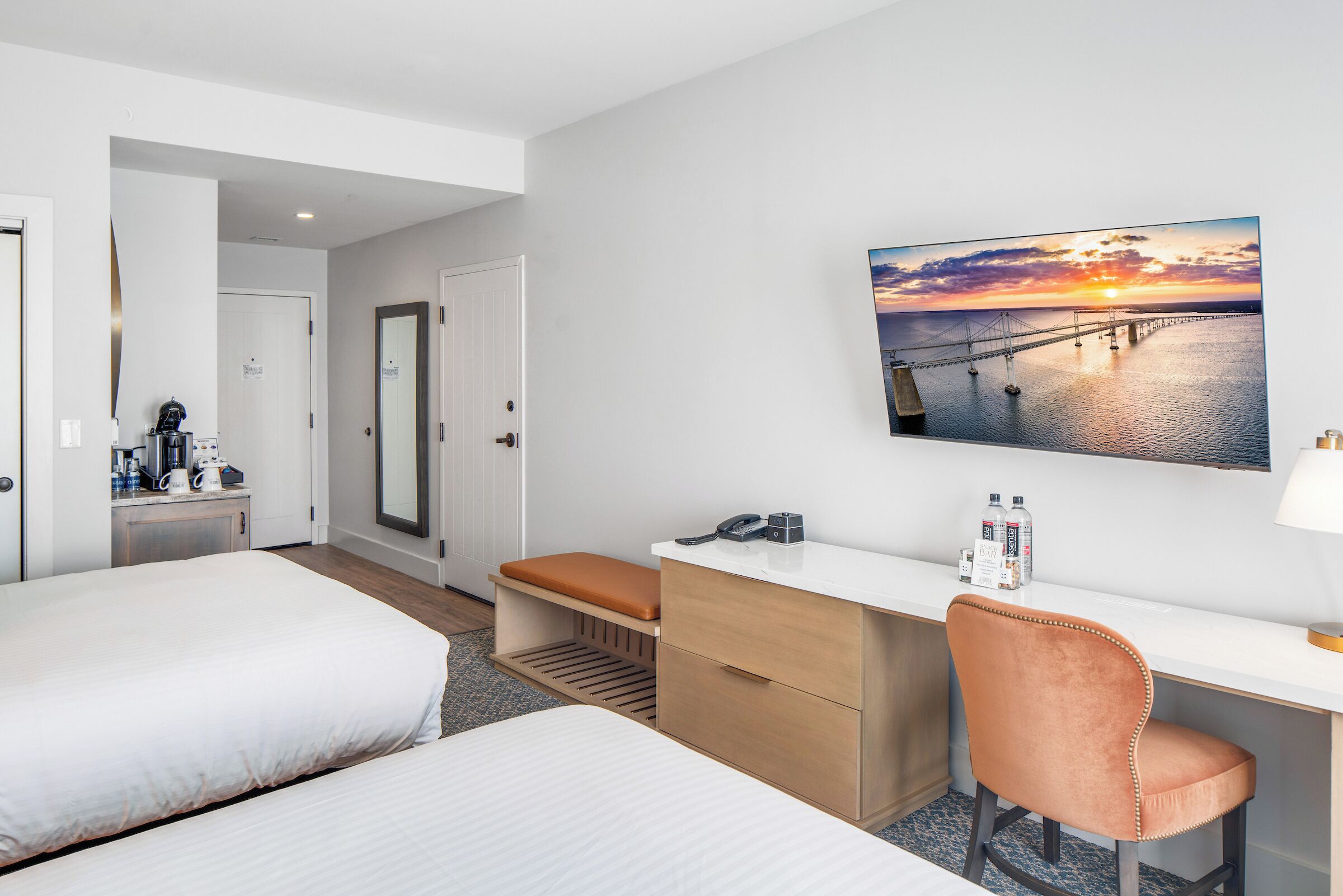 Une chambre d’hôtel avec deux lits, un bureau, une chaise, un coin café et une vue sur le coucher de soleil.