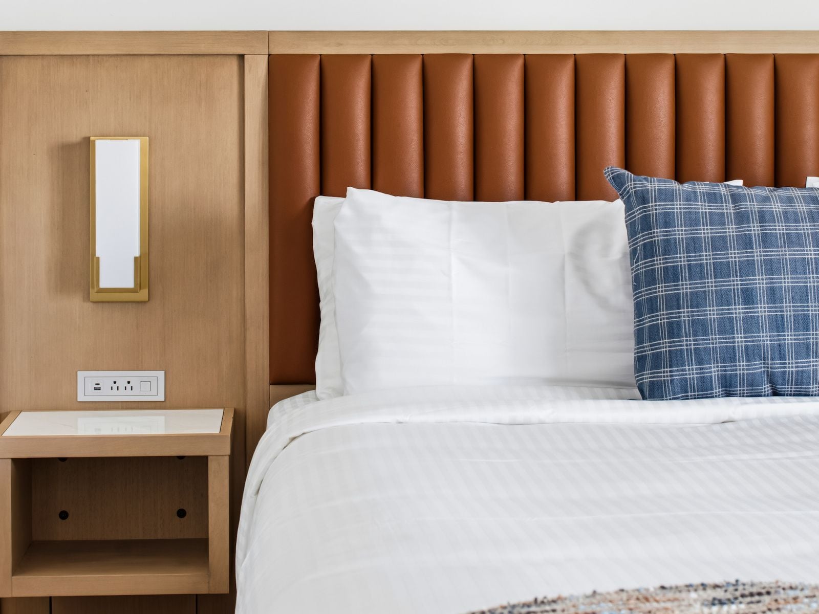 Quarto de hotel com cama, mesa de cabeceira, luminária na parede e tomada.