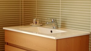 Un baño con tocador de madera, espejo redondo y lavamanos.