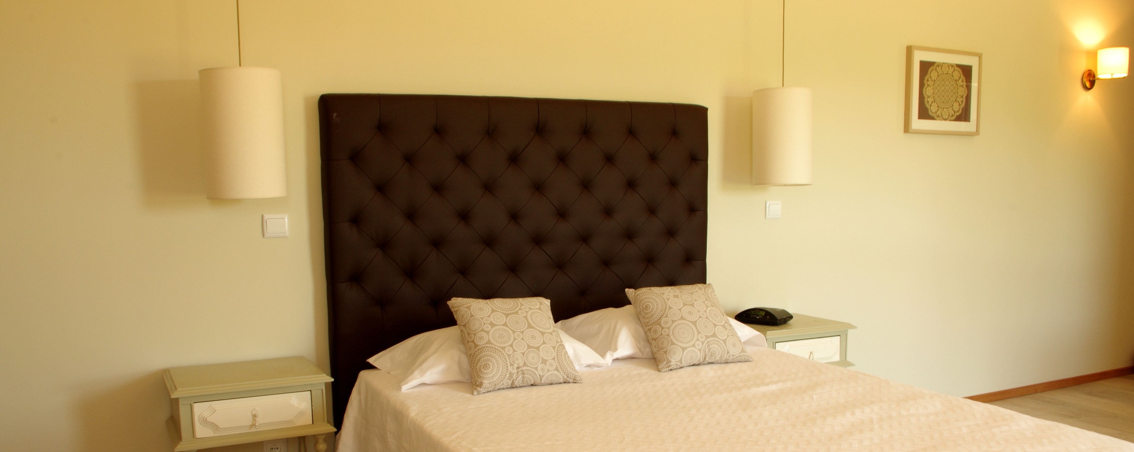 A neatly made bed with a tufted headboard, two bedside tables, and a wall-mounted light fixture.
