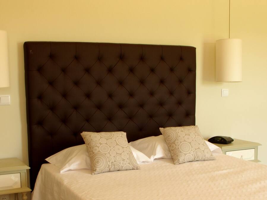 A neatly made bed with a tufted headboard, two bedside tables, and a wall-mounted light fixture.