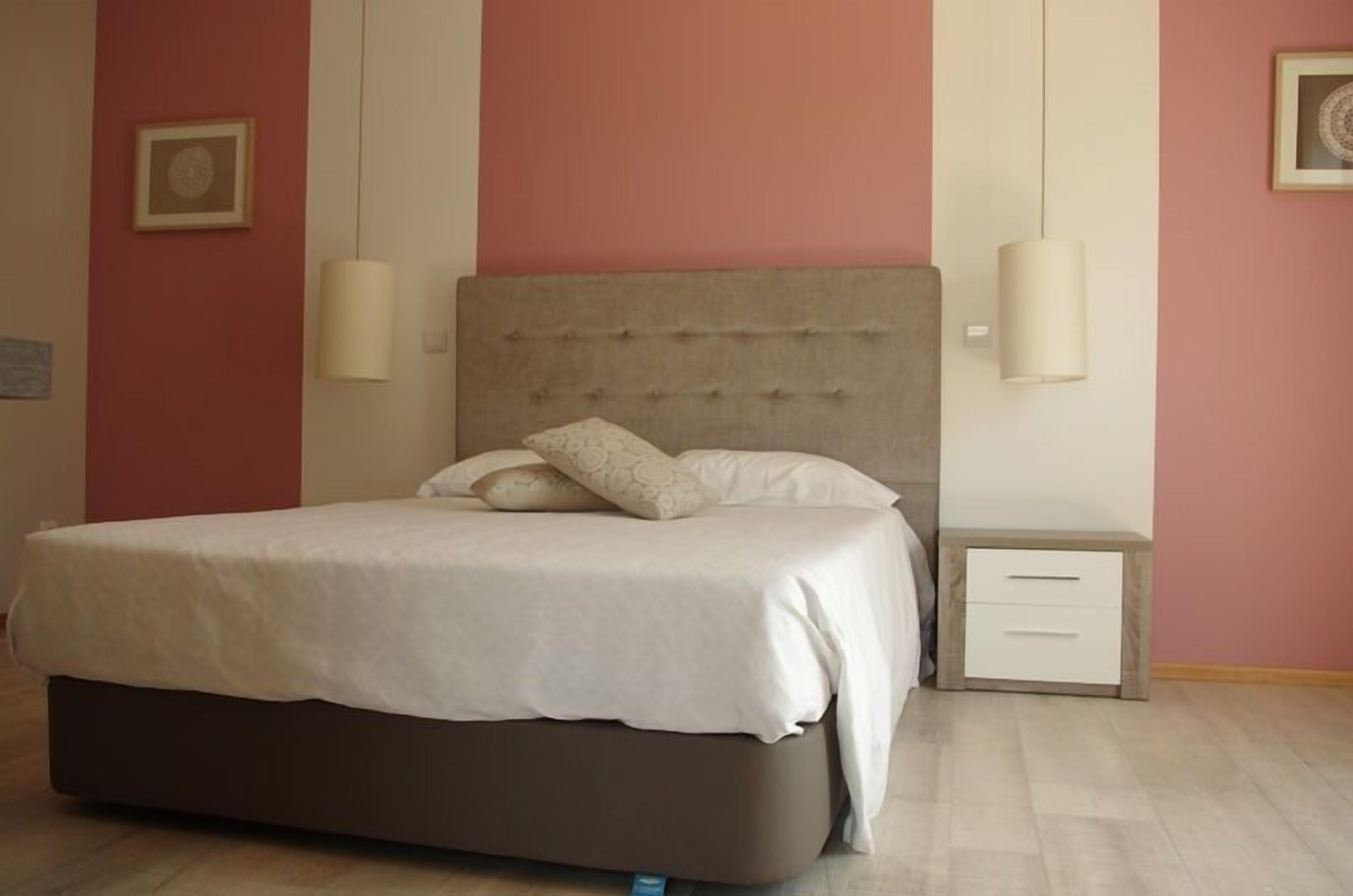 A bedroom with a large bed, a nightstand, and two wall-mounted lamps.
