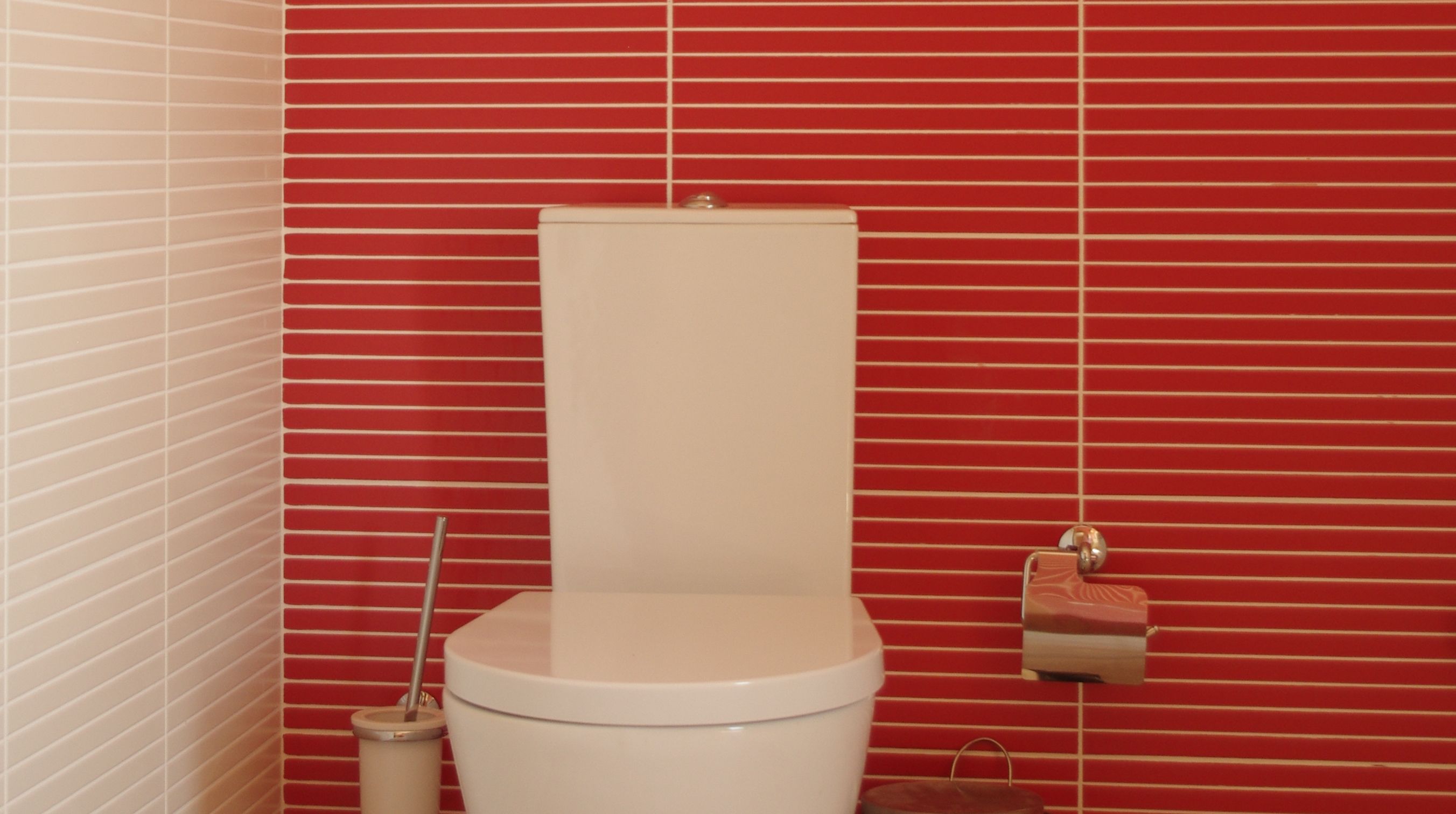 A toilet with a white tank and lid, positioned against a red tiled wall.