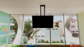 A room with large windows, a flat-screen TV, and bean bags. - Room2Board Hostel and Surf School (Jacó)