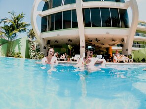 Un espace piscine avec des chaises longues et, au fond, un bâtiment doté de nombreuses fenêtres et de balcons.