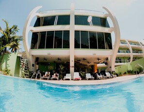 Un hôtel moderne doté d’un espace piscine, avec une structure à deux étages, de grandes fenêtres et un bar-cuisine.
