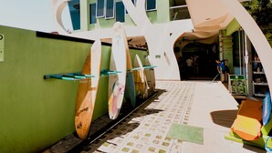 A building with a green exterior and white arches. Inside, there are surfboards leaning against the wall. - Room2Board Hostel and Surf School (Jacó)