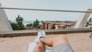A person sitting on a balcony with a view of the beach and buildings. - Room2Board Hostel and Surf School (Jacó)