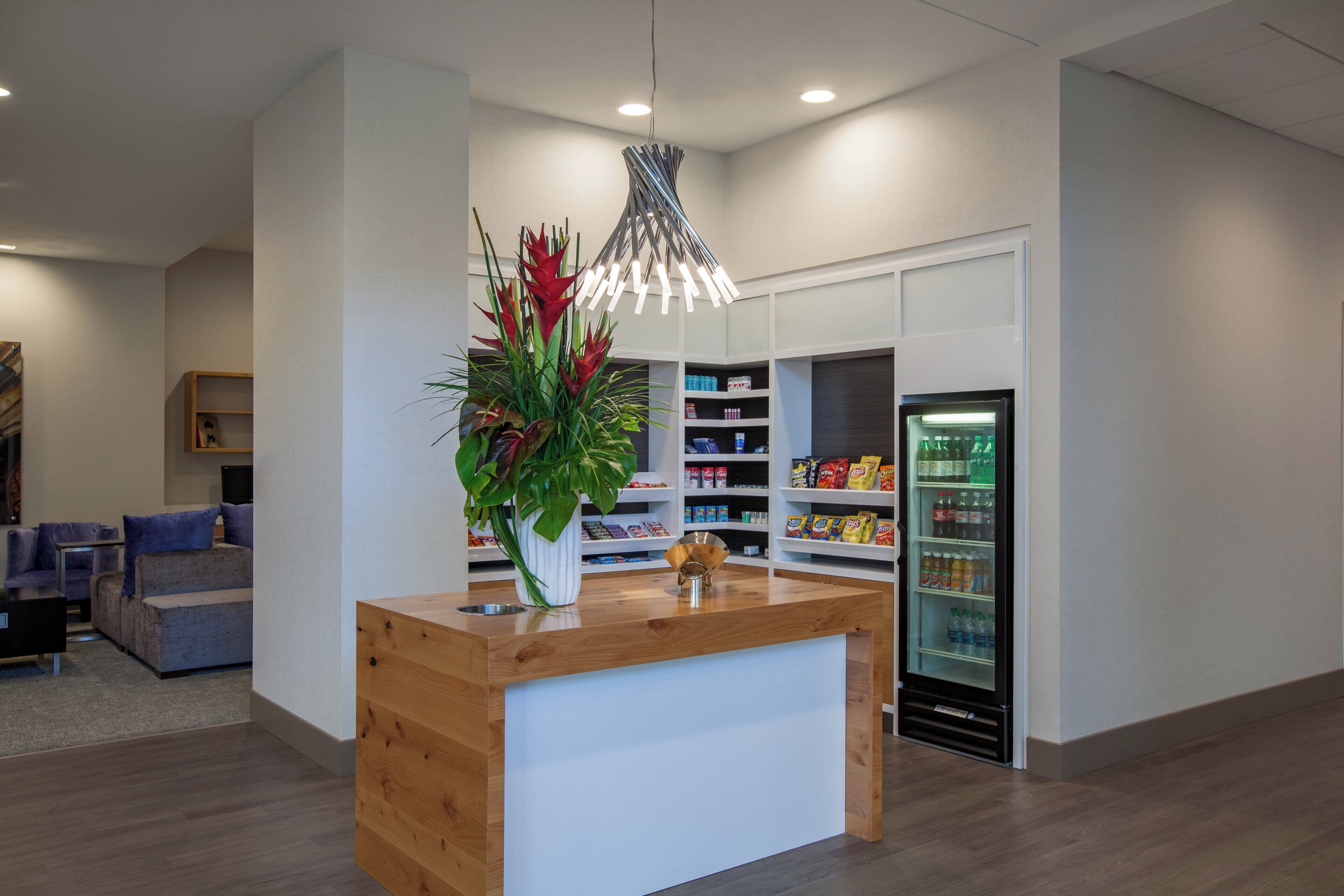 A reception area with a wooden counter, a potted plant, a modern pendant light, and a beverage refrigerator.