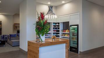 A reception area with a wooden counter, a potted plant, a modern pendant light, and a beverage refrigerator.