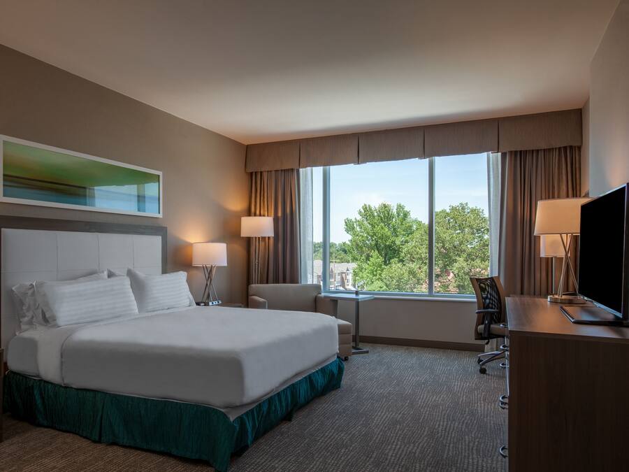 Una habitación de hotel con una cama grande, dos mesitas de noche, un escritorio con silla, un televisor y una ventana con cortinas.