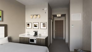 A hotel room with a bed, a vanity with a mirror, a microwave, and framed artwork on the wall.
