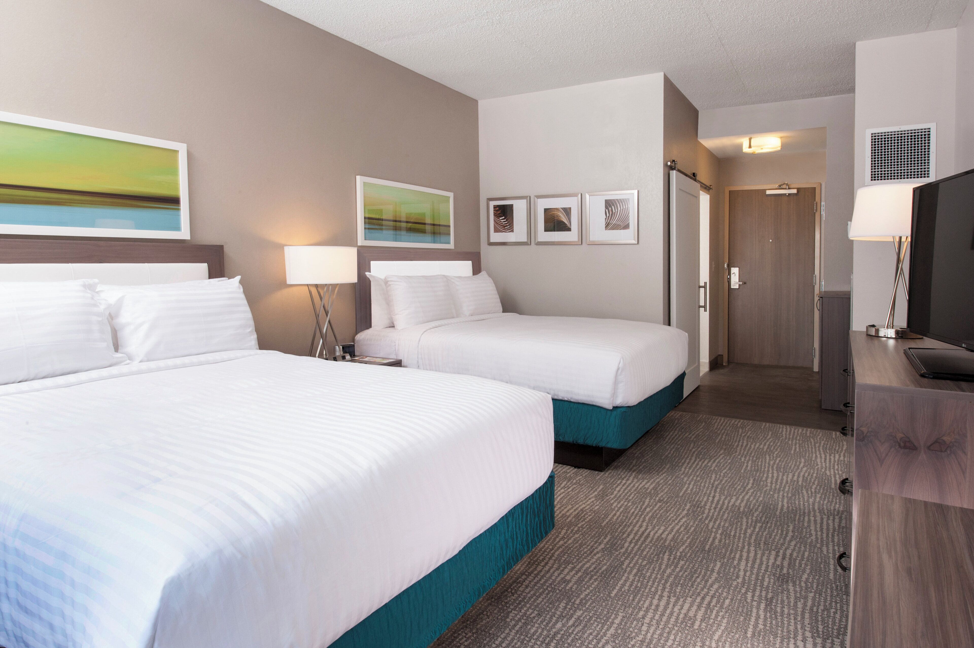 A hotel room with two beds, a TV, a desk, and artwork on the walls.