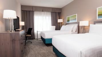 Une chambre d’hôtel avec deux lits, un bureau, une chaise et une lampe.