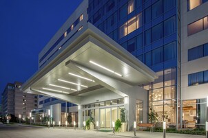 A modern hotel entrance with a covered walkway, glass doors, and a bench.