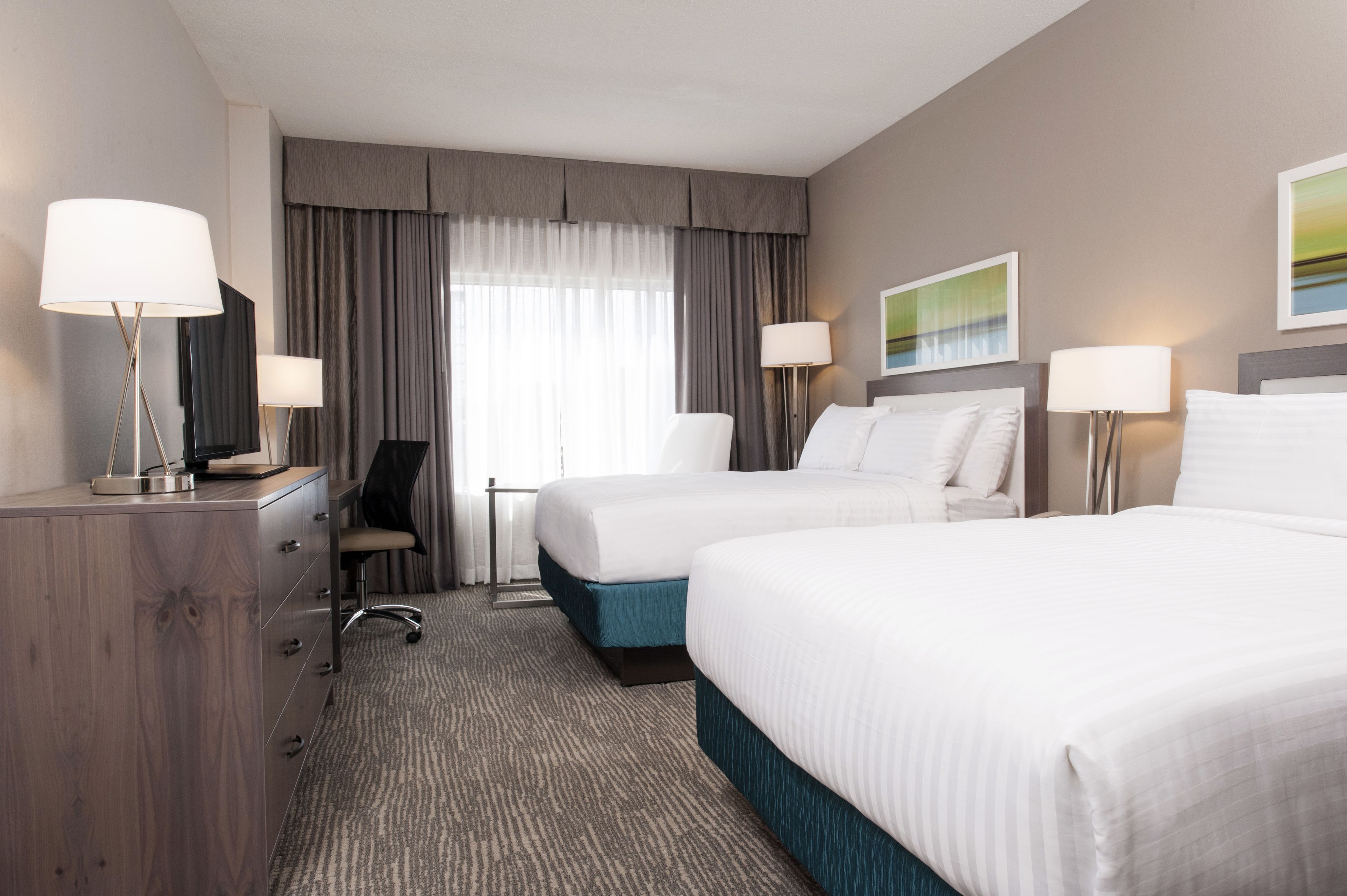 Une chambre d’hôtel avec deux lits, un bureau, une chaise et une lampe.