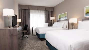 A hotel room with two beds, a desk, a chair, and a lamp.