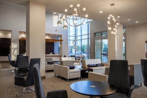 A modern lounge area with sofas, chairs, and a round table, featuring a large window and a unique chandelier.