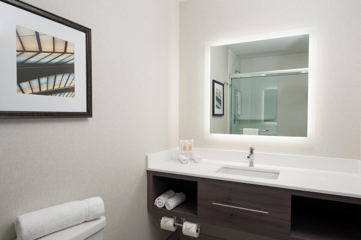 A modern bathroom with a large mirror, white sink, dark wooden vanity, and a framed picture on the wall.