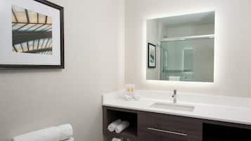 Une salle de bain moderne avec un grand miroir, un lavabo blanc, un meuble-lavabo en bois foncé et un tableau encadré au mur.