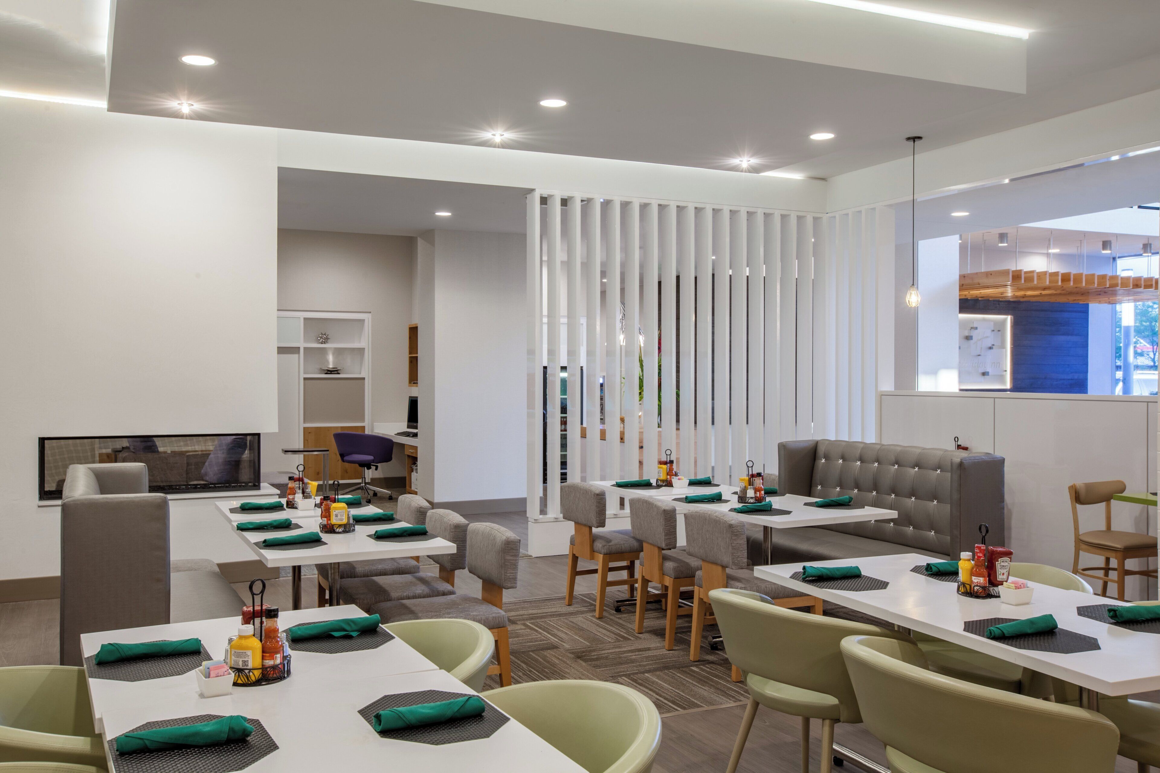 Un espace de restauration moderne dans un hôtel, avec des tables dressées pour les repas, un canapé et un écran de télévision.