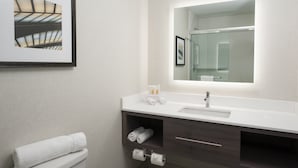 A modern bathroom with a white sink, dark wooden vanity, a framed picture on the wall, and a large mirror above the sink.