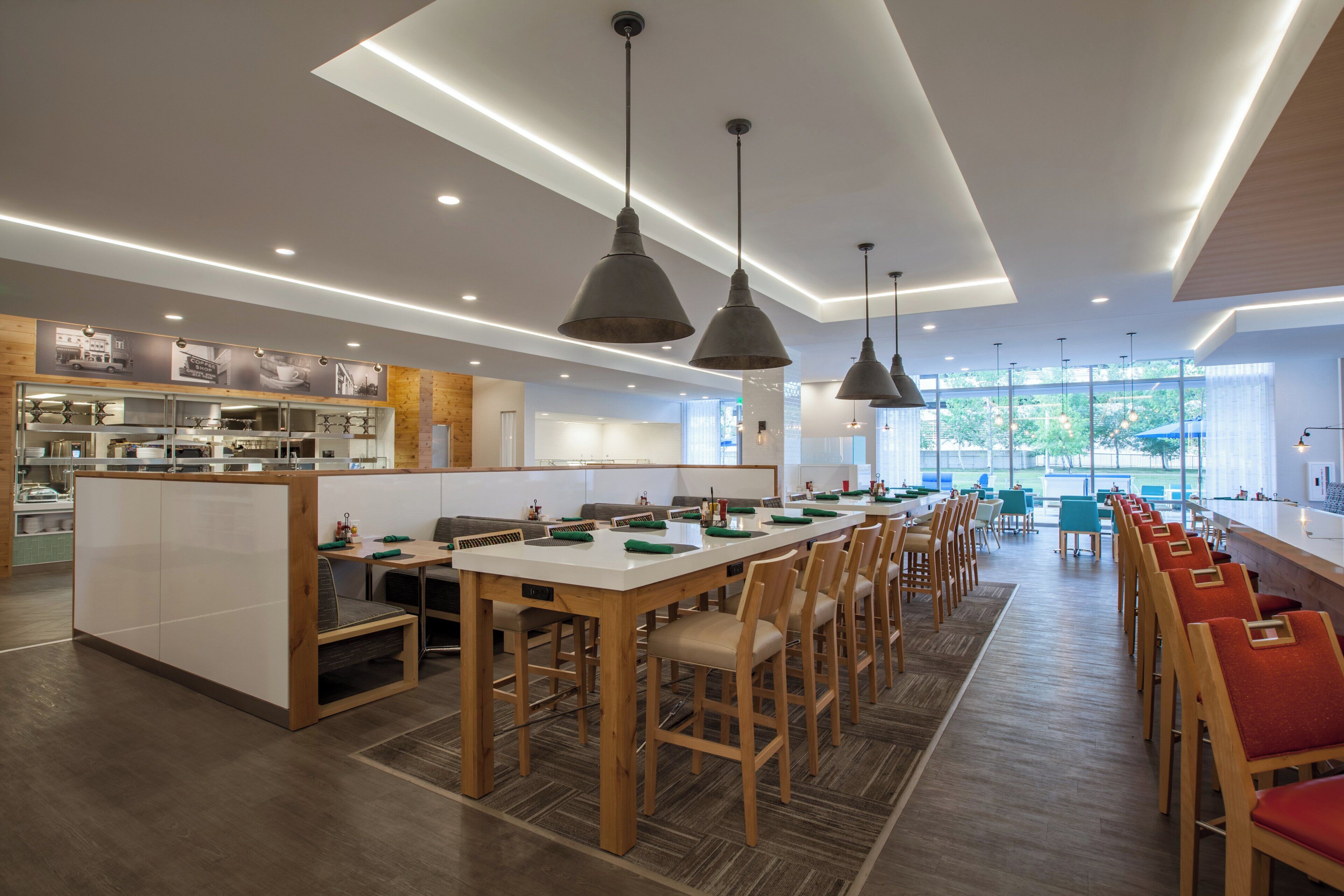 A modern dining area with long tables, wooden chairs, and pendant lighting.