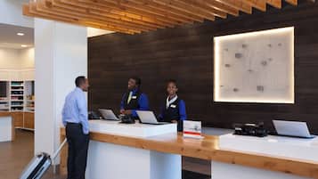 A reception desk with two staff members and a customer, a wooden ceiling, and a wall with a holiday-themed sign.