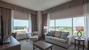 A hotel room with a large window, a sofa, a chair, a coffee table, and a lamp.