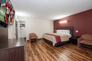 A hotel room with a bed, two armchairs, a desk, a TV, and a wooden floor.