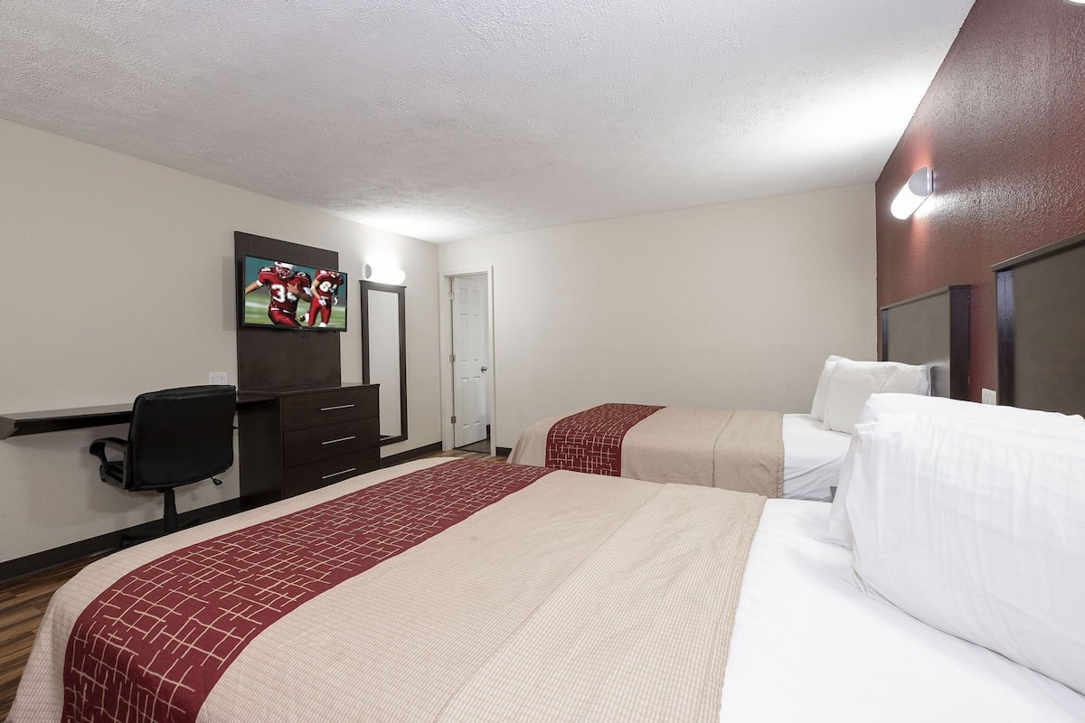 A hotel room with two beds, a desk, a chair, a TV, and a door.