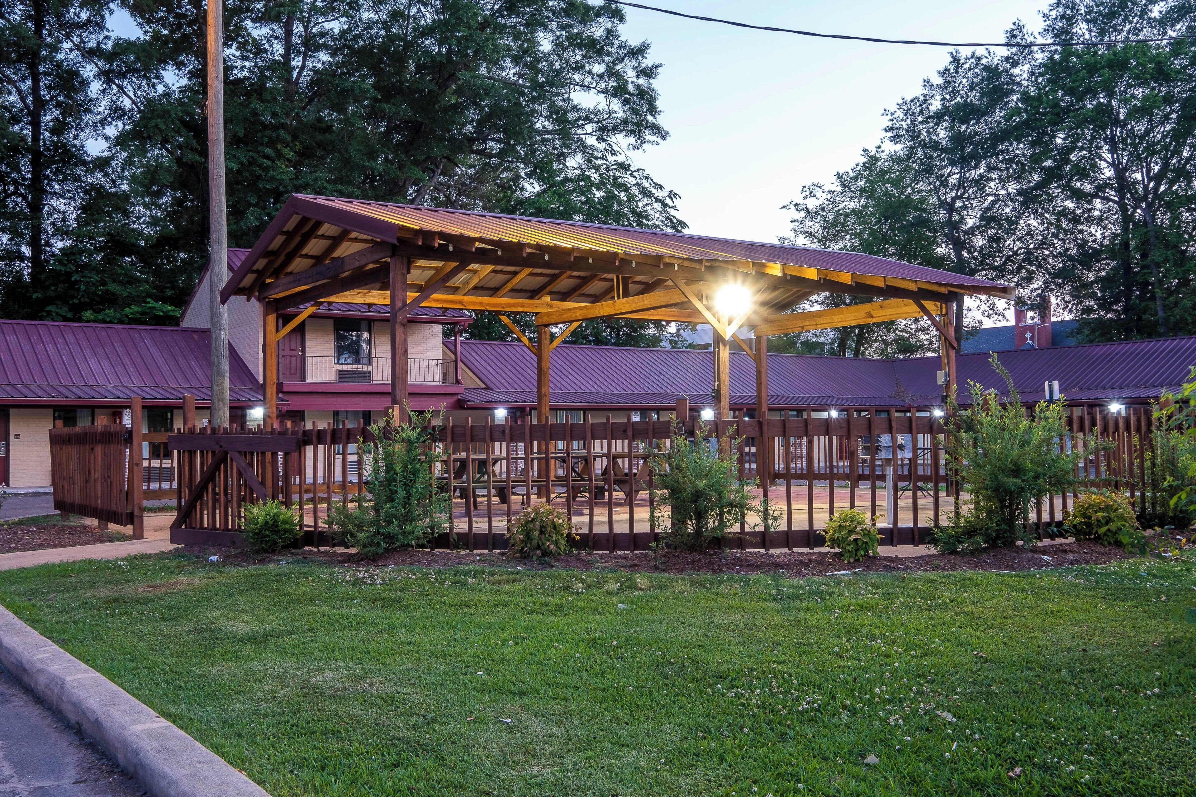 A building with a covered patio area, a fenced playground, and a grassy lawn.