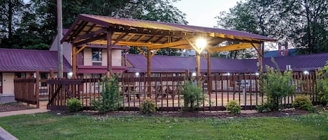 A building with a covered patio area, a fenced playground, and a grassy lawn.
