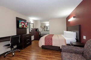 A hotel room with a bed, a desk, a chair, a television, and a mirror.