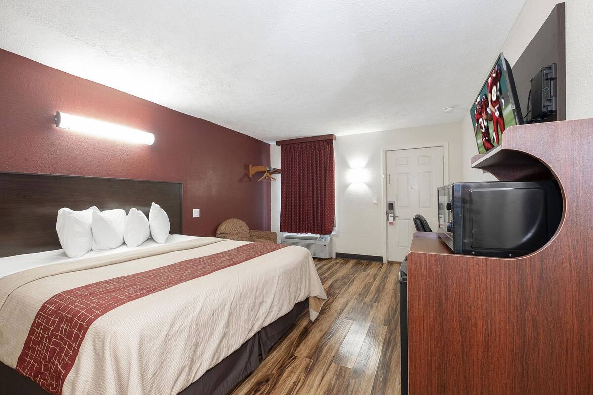 A hotel room with a bed, a TV, a desk, and a door.