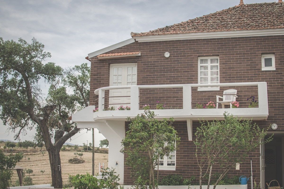A two-story brick house with a balcony, white railings, and a small garden area.