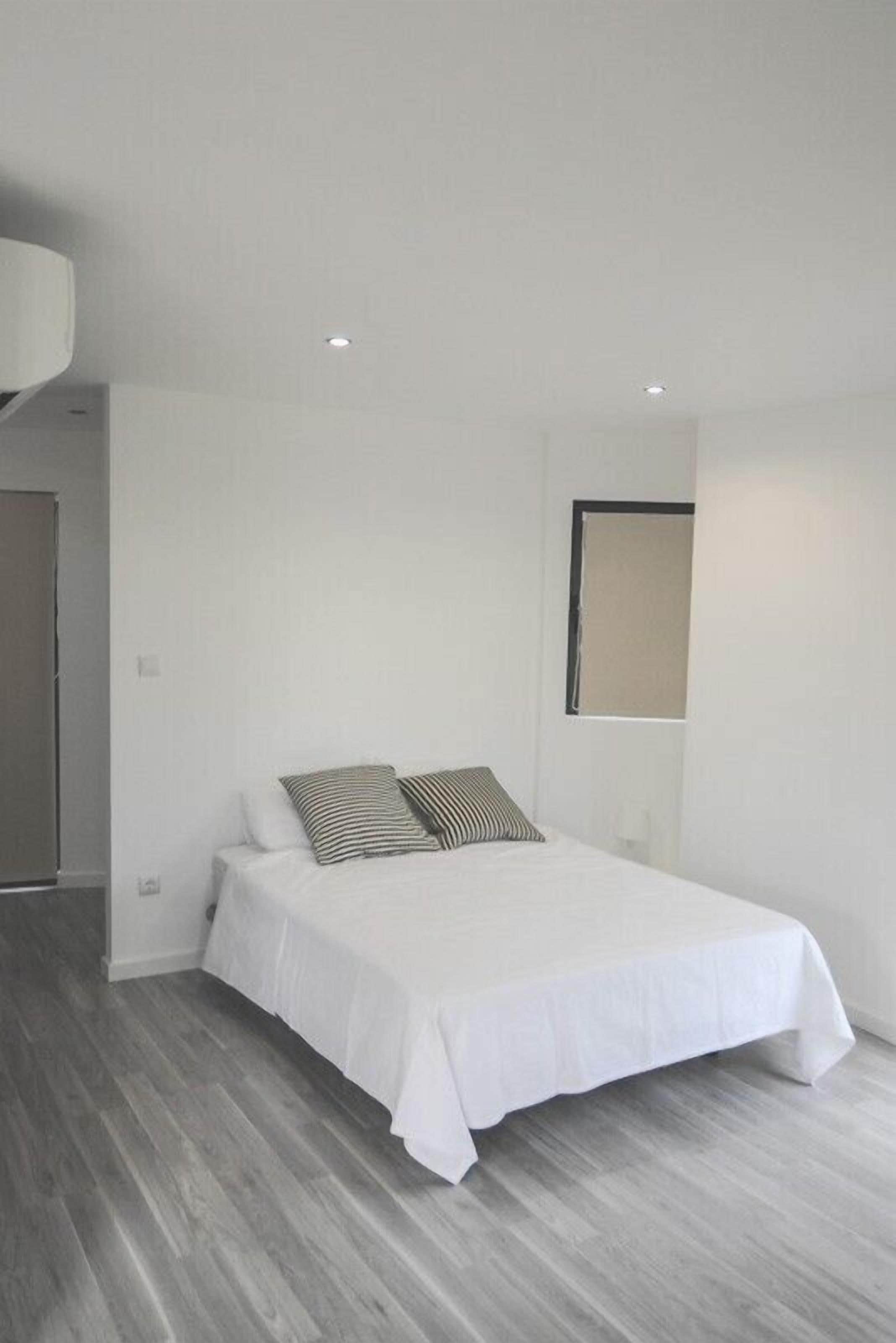 A minimalist bedroom with a single bed, a window, and a wooden floor.
